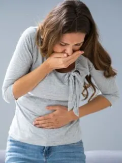 A woman holding her stomach and mouth like she might vomit.